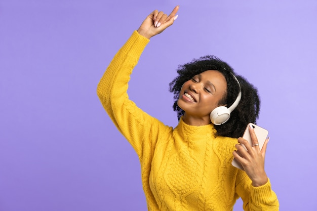 Energized mixed race woman dancing, wears wireless headphones, listens to music, isolated