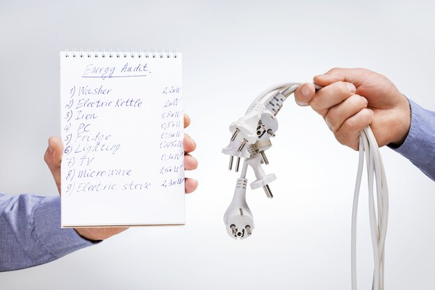 Energy audit concept. Hands holding notebook with text and many electrical wires.