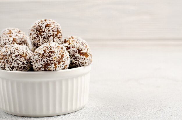 Energy balls of dates, nuts, oats, sprinkled with coconut powder closeup in a white plate on a white table
