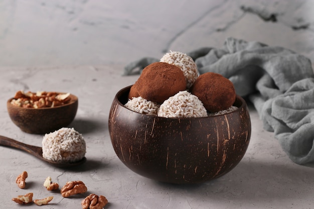 Energy balls of nuts and oatmeals with coconut flakes and cocoa in coconut bowl on gray surface, horizontal format, Closeup