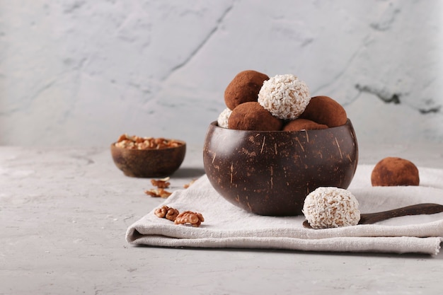 Energy balls of nuts and oatmeals with coconut flakes and cocoa in coconut bowl on gray