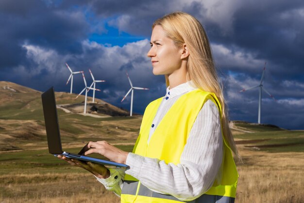 Energy and industry Portrait of a successful female engineer with a laptop on the background of a wind farm