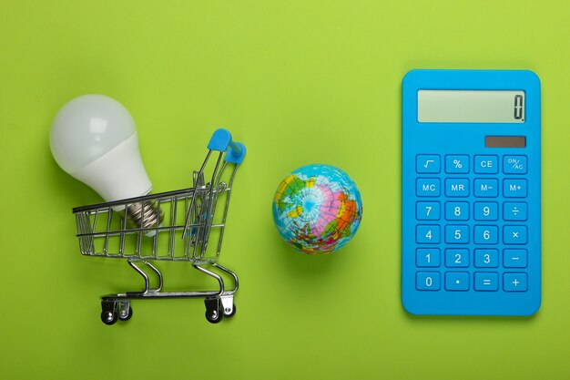 Energy saving. Calculator, shopping trolley with led light bulb and globe on green background. Save planet. Eco concept. Top view