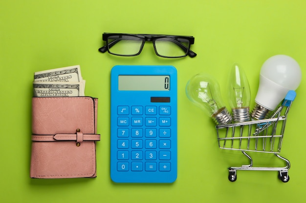 Energy saving concept. Supermarket shopping trolley and light bulbs, calculator and purse on green