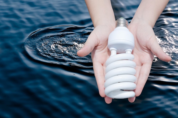省エネのコンセプト暗い水の背景に電球を持っている女性の手手に電球のアイデア
