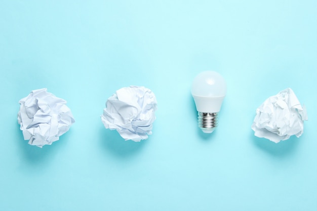 Energy saving light bulb and crumpled paper balls on blue table. Minimalistic business concept, idea. Top view