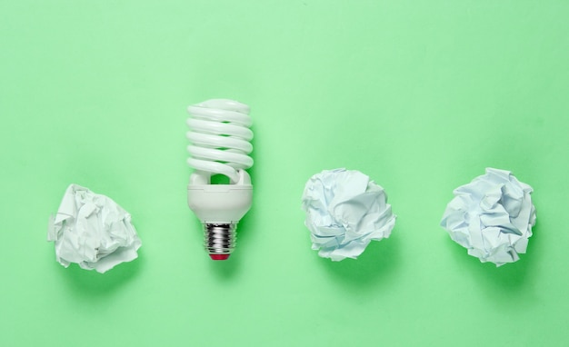 Energy saving light bulb and crumpled paper balls on green background. Minimalistic business concept, idea. Top view