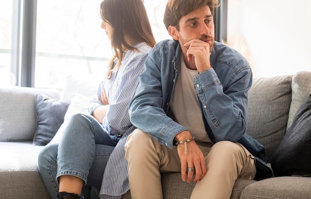 Engaged couple with relationship problems sitting on the sofa with their backs to each other after an argument conflicts in marriage upset couple after a dispute making decision to break up divorce