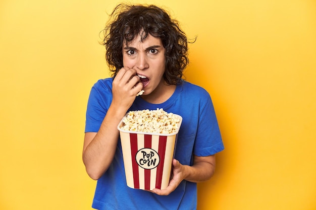 Engaged woman with popcorn watching screen home cinema concept yellow studio backdrop