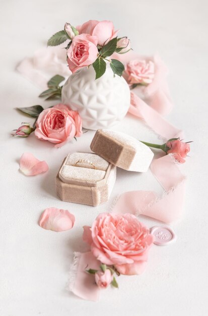 Обручальное кольцо в кремовой бархатной коробке рядом с светло-розовыми розами и бутонами