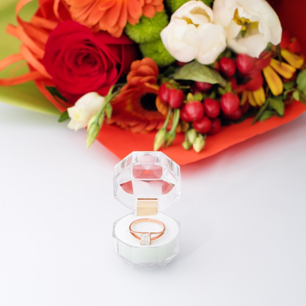 Engagement ring in a gift box with bright bouquet of flowers. The offer to get married. Gift for St. Valentine's Day. Marriage proposal for beloved woman. Symbol of love and marriage.