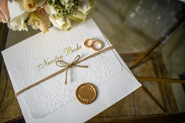 Engagement rings on top of a wedding invitation with a gold seal next to a bouquet of flowers