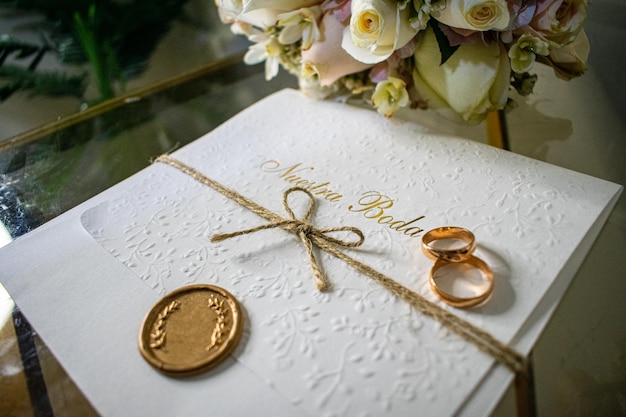 Engagement rings on top of a wedding invitation with a gold seal next to a bouquet of flowers