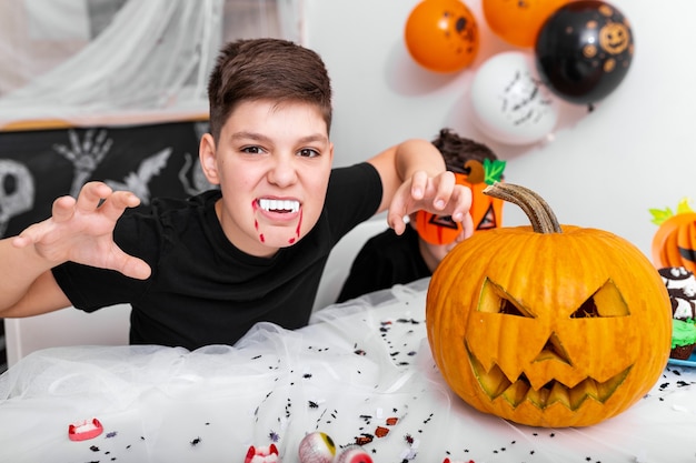 Enge jongen met hoektanden op het halloween-feest. Jack O 'Lantern Halloween-pompoen op tafel