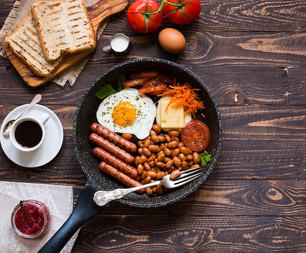 Engels ontbijt. Gebakken eieren, worstjes, bonen, brood toast, tomaten, kaas op een houten achtergrond,