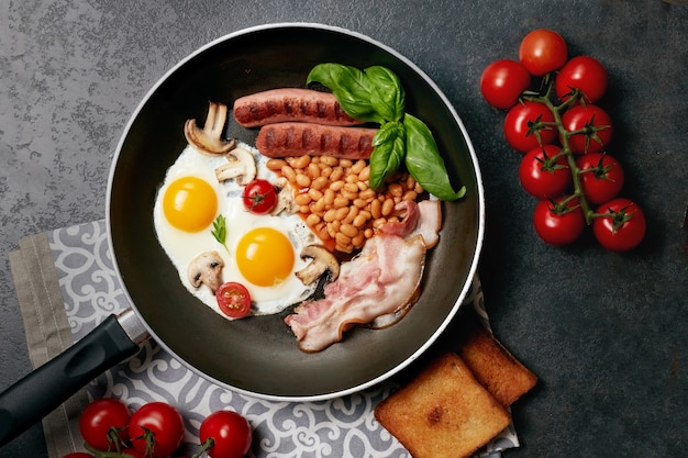 Engels ontbijt in de kookpan met gebakken eieren, worstjes, bonen, tomaten, champignons, spek en toast op houten tafel. Kopieer ruimte. Bovenaanzicht