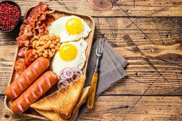 Engels ontbijt in een houten dienblad met gebakken eieren, worstjes, spek, bonen en toast. houten tafel. bovenaanzicht.