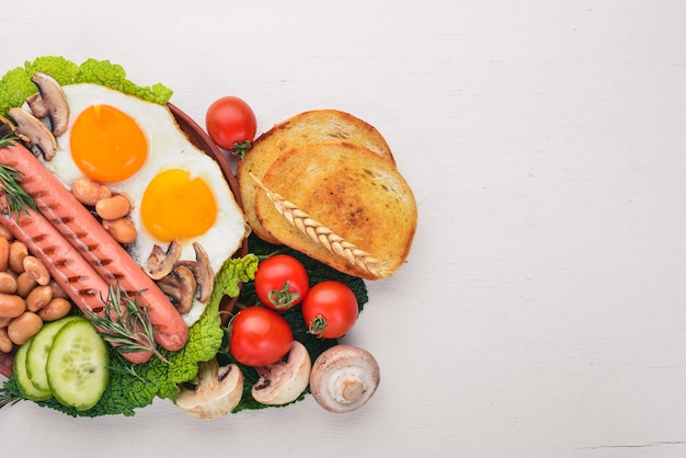 Engels ontbijt tomaten worstjes bonen champignons Eggstoast en kruiden bovenaanzicht op een witte houten achtergrond