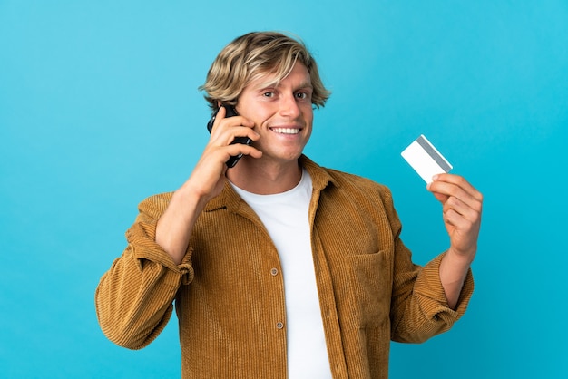 Engelse man over geïsoleerde blauwe achtergrond die een gesprek met de mobiele telefoon houdt en een creditcard houdt