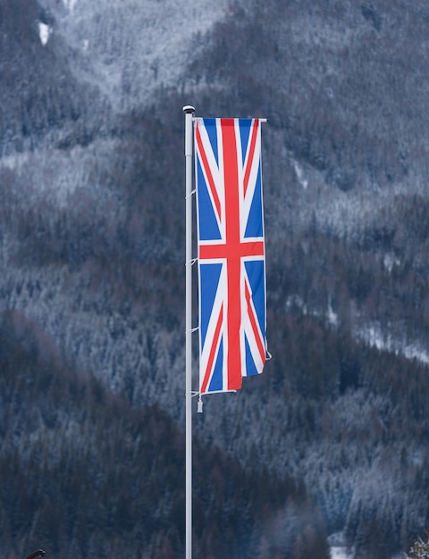 Engelse vlag zwaaiend door de wind tegen bos bedekt met sneeuw