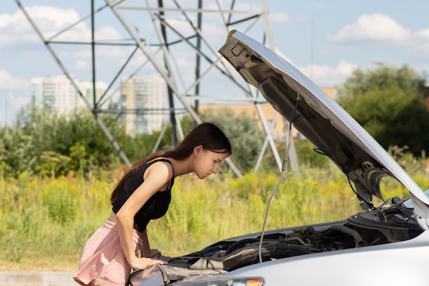 エンジンの問題 女性は車のフードの下を見て 故障の理由を見つけようとします