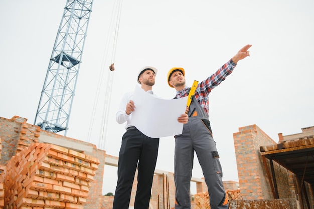 Engineer and builder in hard hats discussing blueprint on construction site