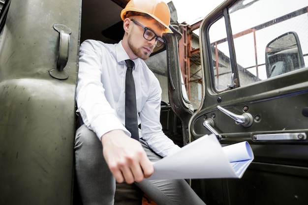 Engineer builder in a helmet holds drawings at construction site