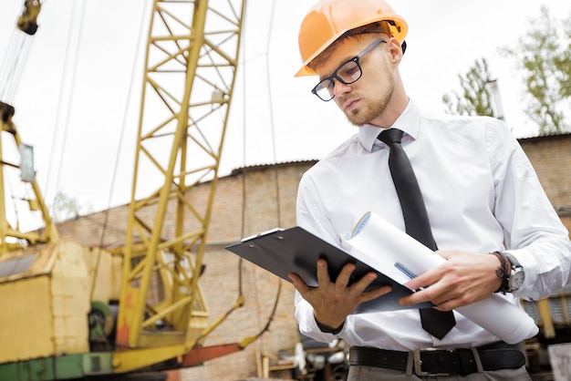 Engineer builder in a helmet holds drawings at construction site