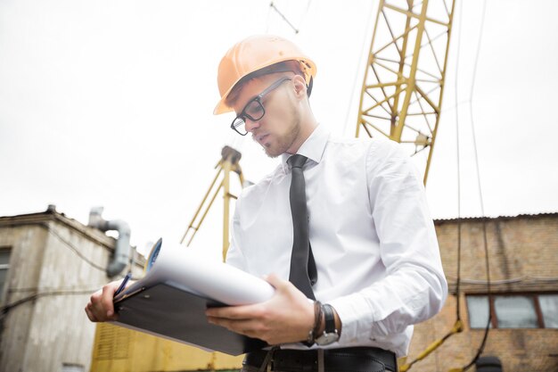 Engineer builder in a helmet holds drawings at construction site