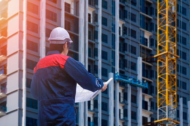 Engineer builder holding project blueprint with looking at building structure in construction site