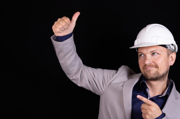 Engineer, builder, in a white helmet on a dark background. Hand gestures.