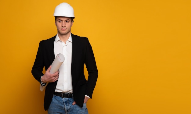 Engineer businessman. Close-up photo of a serious businessman in smart casual outfit and helmet, who is holding a blueprint in his right hand and looking aside.