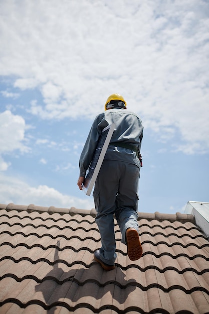 屋根の上を歩くときにソーラーパネルを運ぶエンジニアの後ろからの眺め