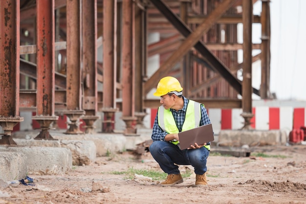Фото Инженер проверяет проект на объекте человек в шапке с ноутбуком на строительстве инфраструктуры