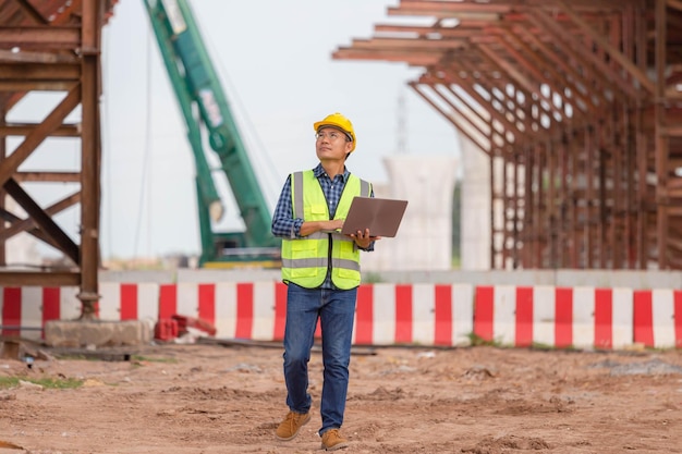 Engineer checking project at the building site man in hardhat\
with laptop at the infrastructure construction site