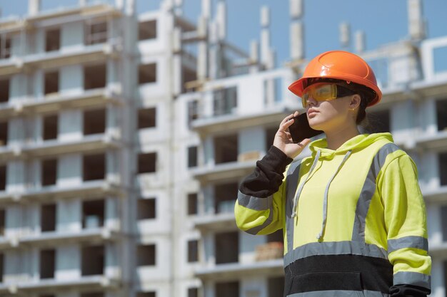 An engineer discusses the construction process by phone against the background of a multi-storey building under construction