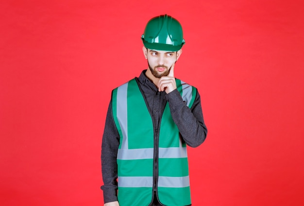 Engineer in green uniform and helmet thinking and planning. 