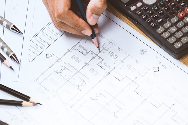 Engineer hand drawing plan on blue print at desk.