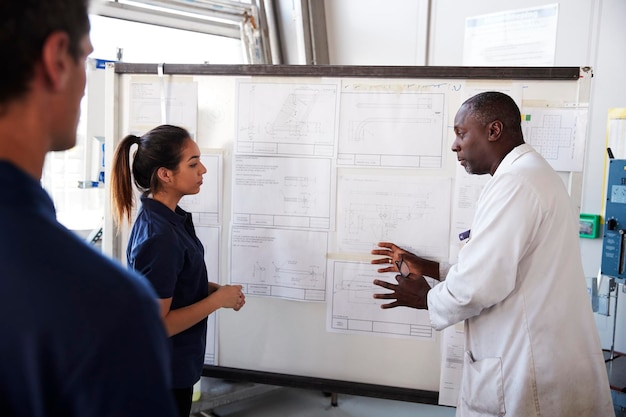 Engineer instructs two apprentices at white board close up