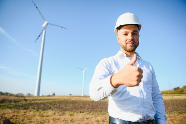 Engineer is checking energy production on wind turbine. Worker in windmills park in helmet.