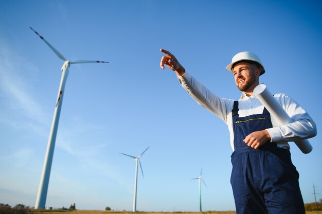 Engineer is checking energy production on wind turbine. Worker in windmills park in helmet.