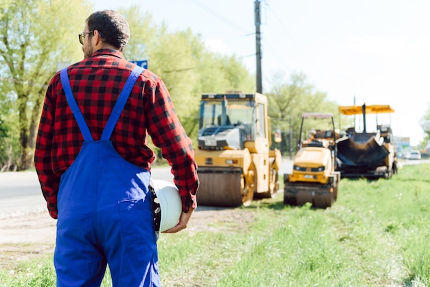 Foto ingegnere ordina ai lavoratori di lavorare in sicurezza in cantiere, i lavoratori mettono l'asfalto sulla strada