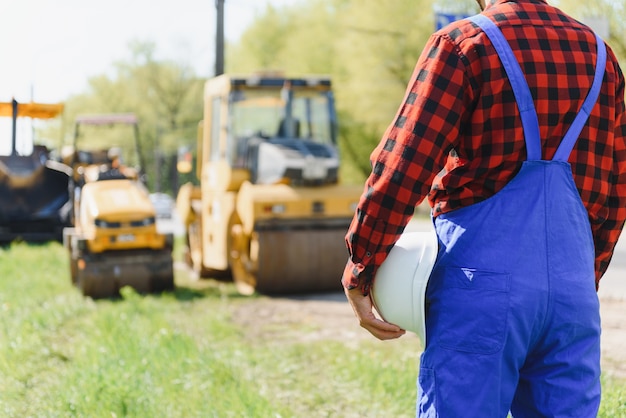 Foto ingegnere ordina ai lavoratori di lavorare in sicurezza in cantiere, i lavoratori mettono l'asfalto sulla strada