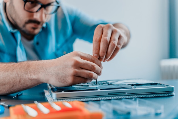 Foto l'ingegnere ripara il computer portatile con il cacciavite. primo piano.