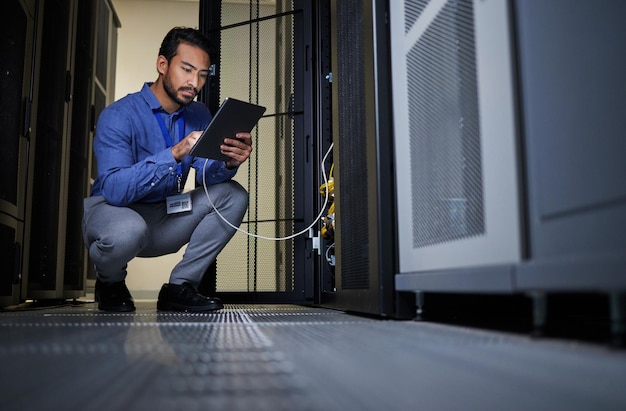 Ingegnere sala server e uomo con tablet per la manutenzione del cavo di connessione al database o l'aggiornamento del software di notte la sicurezza informatica lo cabla e codificatore maschio con tecnologia per il networking nel data center