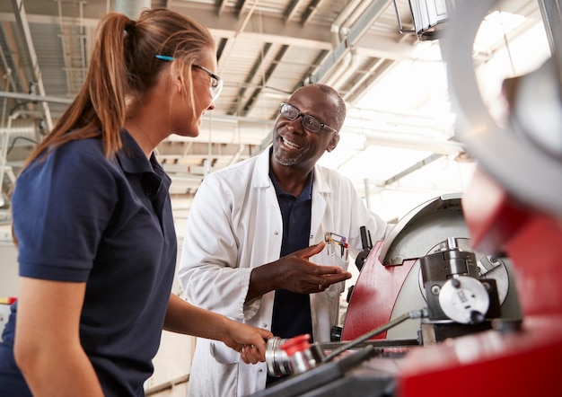 Photo engineer talking to female apprentice by machinery close up