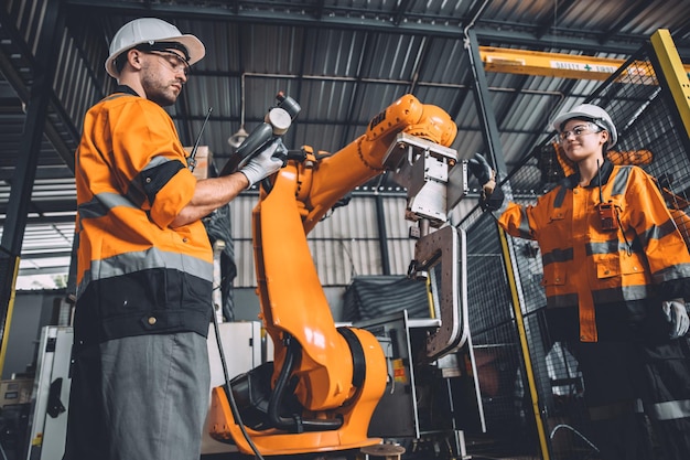 Engineer team service robot welding working in automation factory People worker in safety suit work robotic arm software programming or replacing part in automated manufacturing industry technology