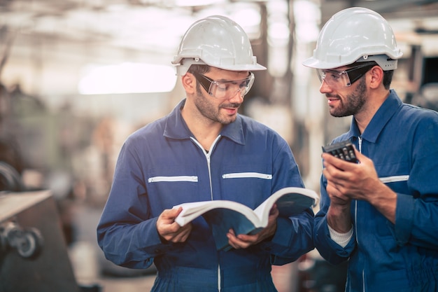 Engineer team talking together teach and learn engineering technical about using machine with open instruction manual text book in factory workplace.