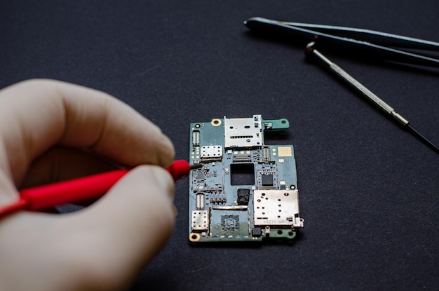 An engineer technician holds a chip and tools for repairing electronic gadgets on a black background Repair of mobile phones