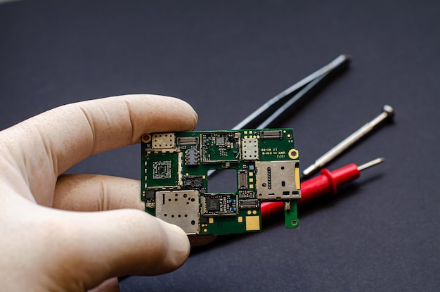 An engineer technician holds a chip and tools for repairing
electronic gadgets on a black background repair of mobile
phones